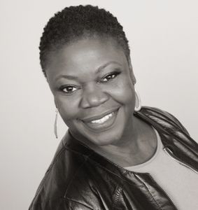 Smiling woman with short hair wearing a leather jacket and hoop earrings.
