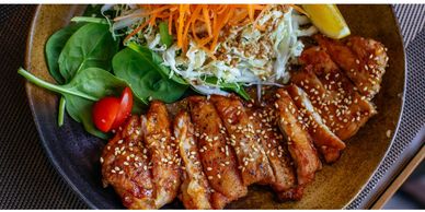 Grilled sesame chicken with fresh salad and lemon wedge on a plate.