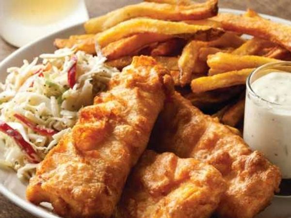 Plate of crispy fish and chips with coleslaw and tartar sauce.