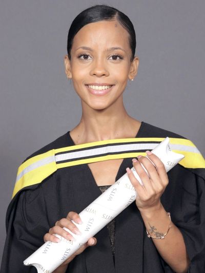 Young woman in graduation gown holding a diploma and smiling.