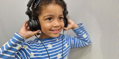 Young child wearing headphones and smiling, enjoying music.
