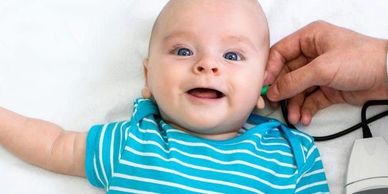 Smiling baby in a blue striped shirt getting a health checkup with a stethoscope.