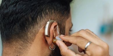 Person adjusting a hearing aid behind their ear.