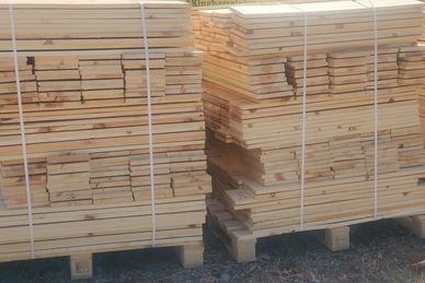 Stacks of neatly bundled wooden planks on pallets outdoors.