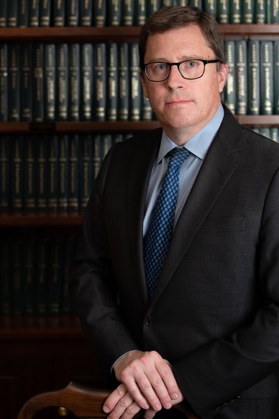 Man in suit and glasses standing in front of law bookshelves.