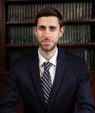 Professional man in suit sitting in front of bookshelves.
