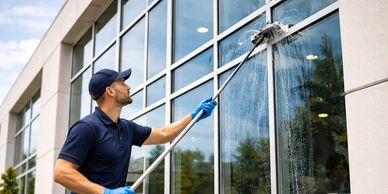 A man in blue uniform cleaning large glass windows.