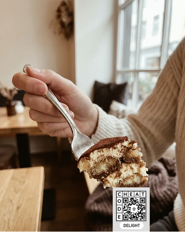 Close-up of a hand holding a fork with tiramisu dessert.