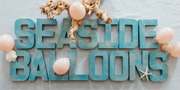 Blue wooden letters spelling 'SEASIDE BALLOONS' with balloons and seashell decorations.