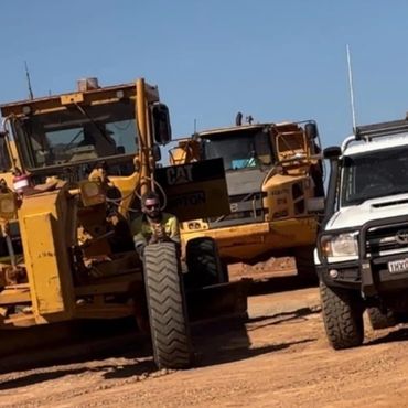 Construction vehicles and a white utility vehicle parked on a dirt road under clear blue sky.