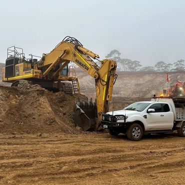 A Komatsu excavator and a white pickup truck at a construction site.