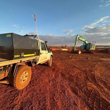 Utility truck and excavator on red dirt at a construction site during sunset.