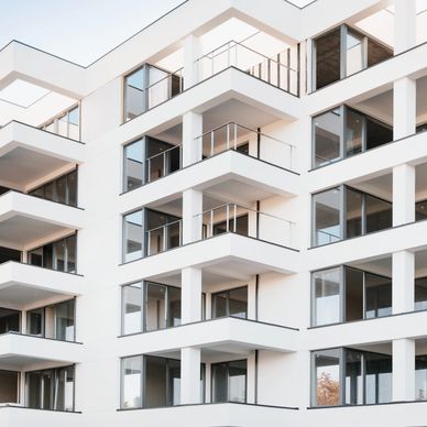 Modern white apartment building with glass balconies and large windows.