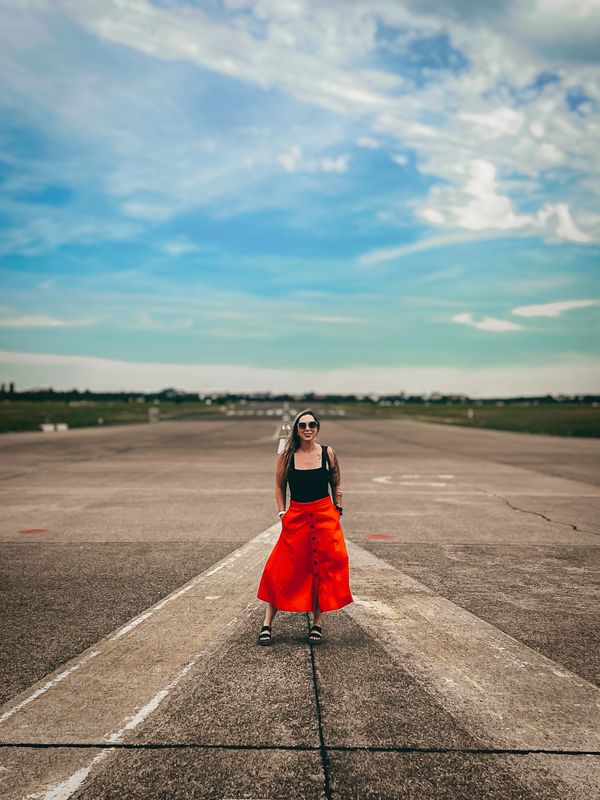 Woman in a red skirt standing on a runway under a blue sky.