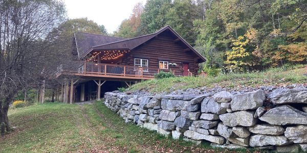 Cozy log cabin with string lights on a hillside surrounded by autumn trees.