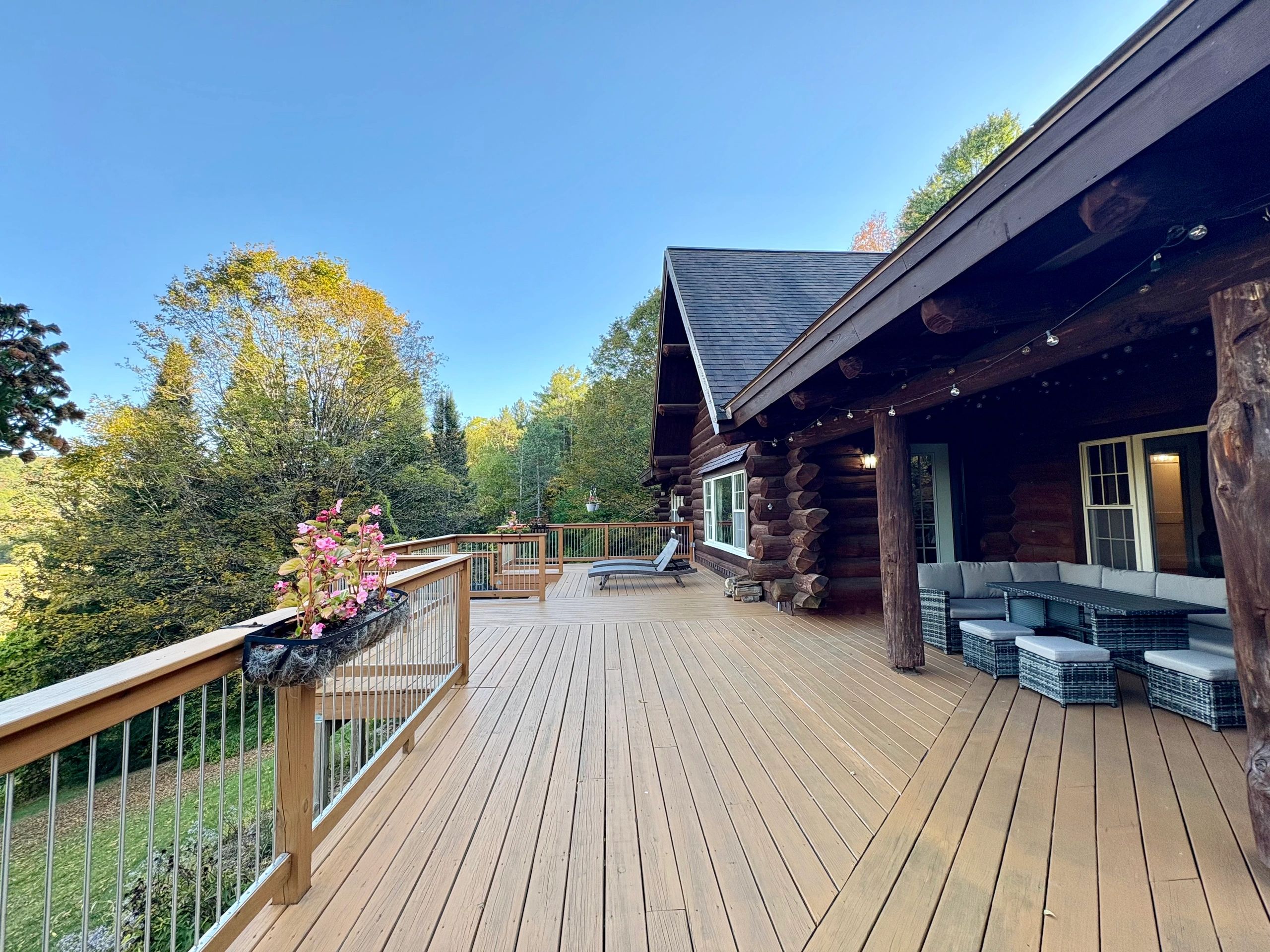 Spacious wooden deck attached to a rustic cabin surrounded by trees.