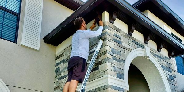 Man on ladder doing home maintenance on house exterior.