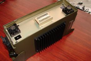 Military-grade electronic device with connectors and heat sink on a wooden table.