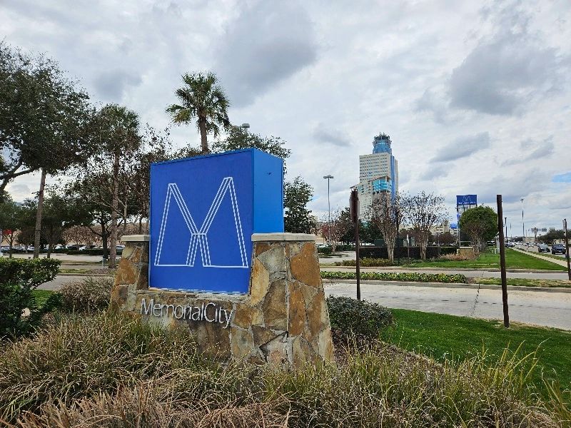 The Memorial City sign with the Memorial Hospital in the distant background. Blue sign with stone.