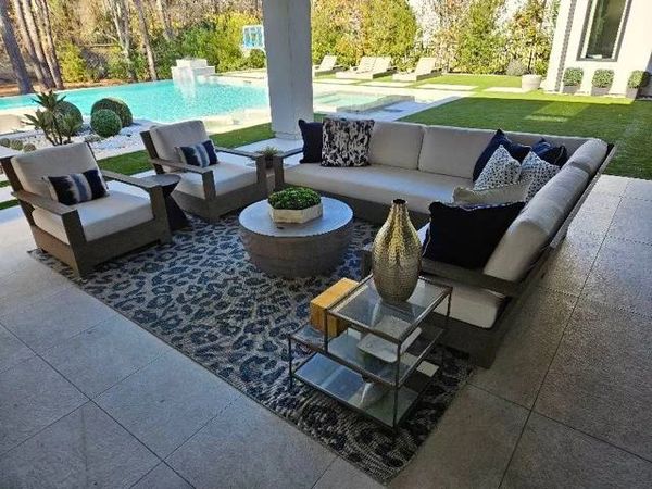 A patio sectional and two chairs with white outdoor cushions and blue pillows. A large backyard pool