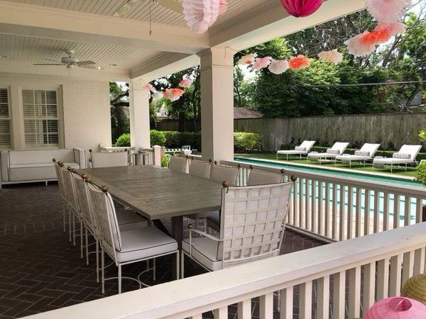 An outdoor dining table with white sunbrella cushions on a patio overlooking a pool and 5 lounges.