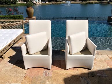 Two outdoor dining chairs with white Sunbrella fabric in front of an infinity pool and lake.