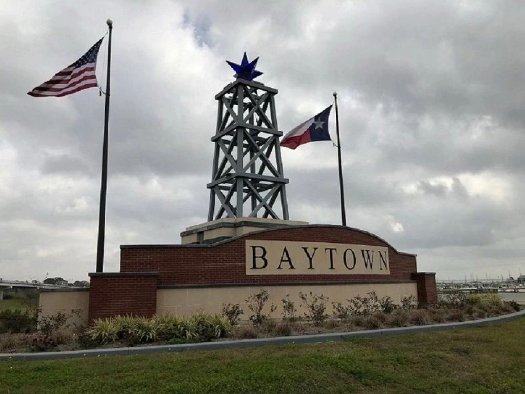 The Baytown city sign with an oil rig and an American flag and Texas flag on either side in Baytown,