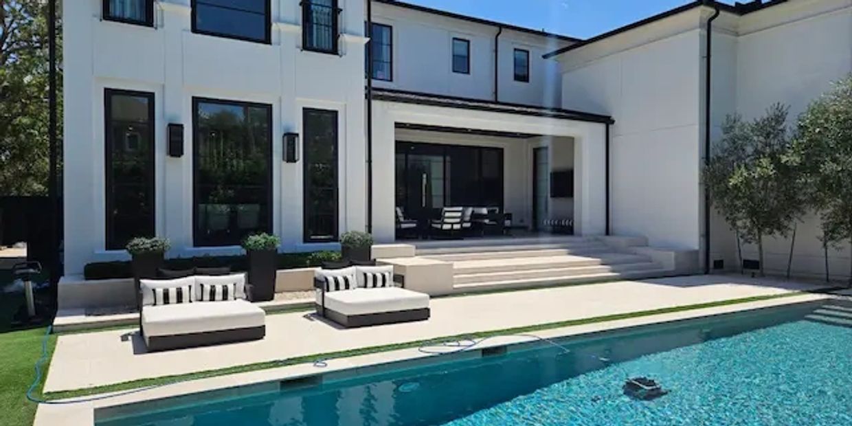 Two large designer patio lounge chairs by the pool in the backyard of a beautiful home