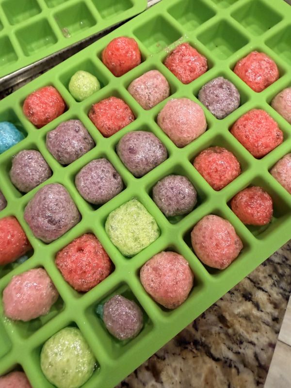 Colorful frozen balls in a green ice cube tray.