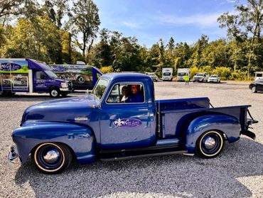 Classic blue Chevrolet pickup with Keith Lott's Plumbing logo and two smiling passengers inside.