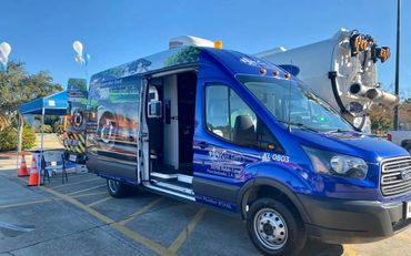 Blue mobile service van parked with an open door and nearby tent setup.