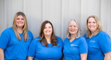 Four women in matching blue shirts smiling in front of a gray wall.
