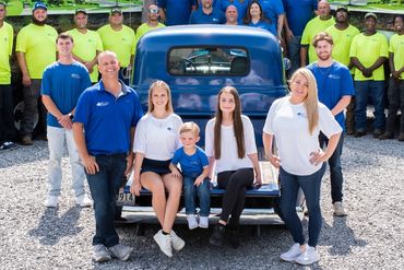 A large group of plumbers posing in front of company trucks outdoors.