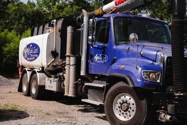 Blue and white Keith Lott's Plumbing vacuum truck parked on gravel.