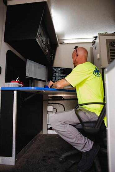 Man in neon yellow shirt working on computer in a compact tech workspace.