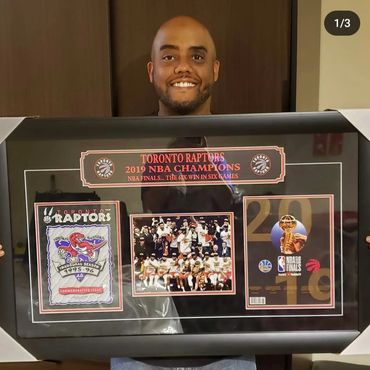 Randy Bowen smiling and holding a framed 1st edition Toronto Raptors game program.