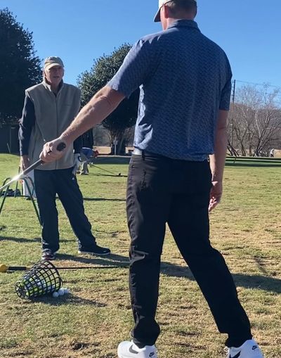 Two men practicing golf swings on a sunny day at a driving range.