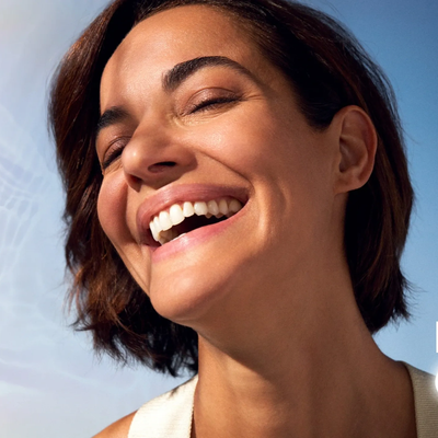 Close-up of a woman smiling joyfully against a blue sky.