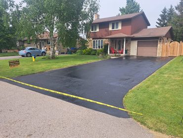 Newly sealed driveway in front of a house with caution tape.