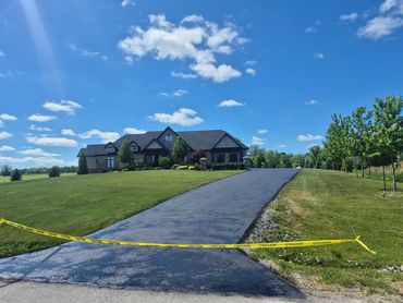 Newly paved driveway with caution tape in front of a suburban house.