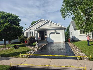 Freshly sealed driveway with caution tape in front of a house.
