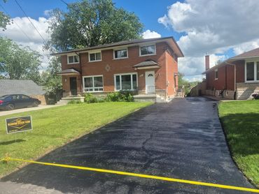 Brick duplex with freshly paved driveway and green lawn.