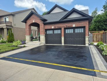 Freshly paved driveway with caution tape in front of a modern brick house.