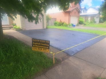 Freshly sealed driveway with a Blacktop Rescue Team sign.