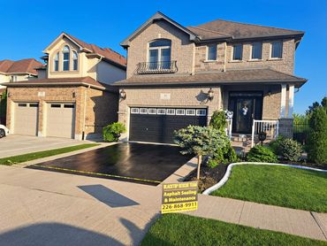 Newly sealed asphalt driveway in front of a house.