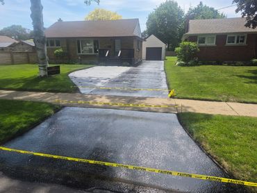 Freshly sealed driveway with caution tape in front of a suburban house.