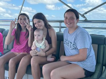 Four kids sitting on a boat, smiling and enjoying a sunny day on the water.