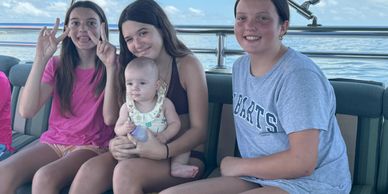 Four kids sitting on a boat, smiling and enjoying a sunny day on the water.