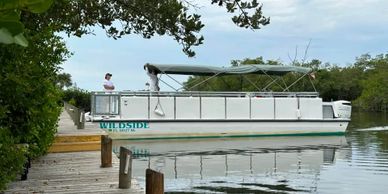 A white boat named Wildside docked by a wooden pier with two people onboard.