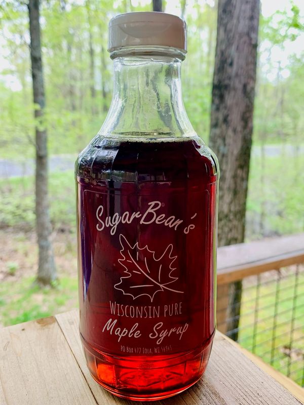 A bottle of SugarBean's Wisconsin pure maple syrup on a wooden surface.